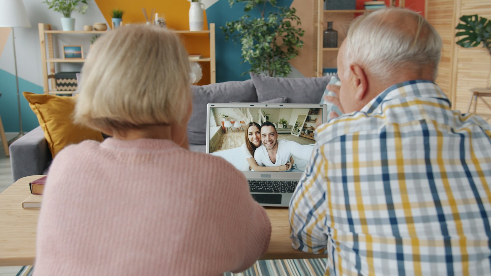 An older couple on their couch smile and wave on a video call with family.